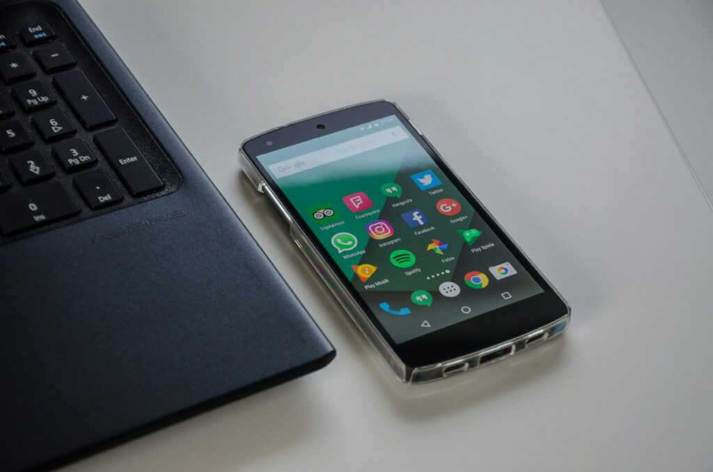 Smartphone on a table showing various social media apps beside a laptop keyboard.